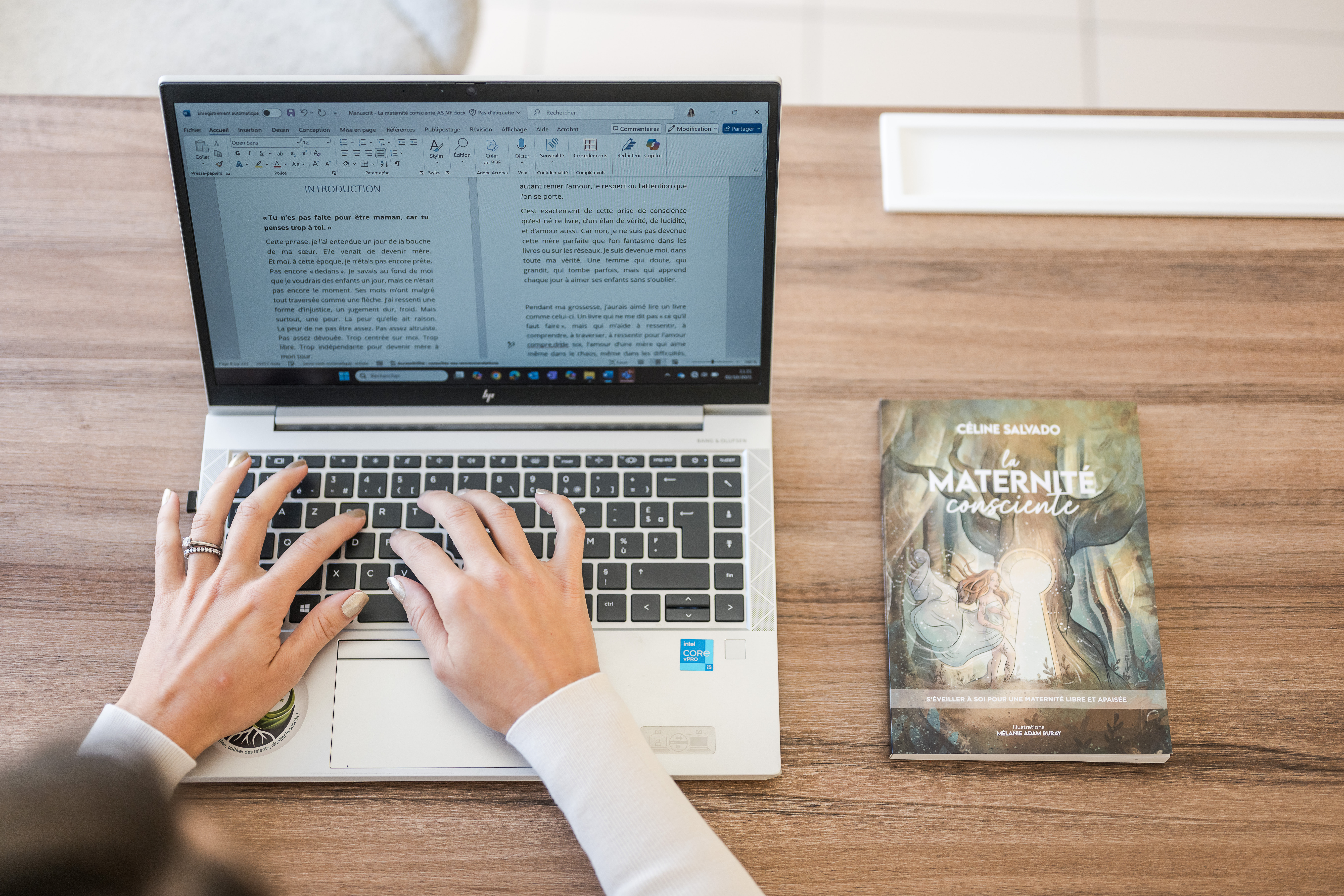 Céline Salvado en pleine rédaction de son livre sur son ordinateur, concentrée et inspirée, dans une atmosphère douce et lumineuse.